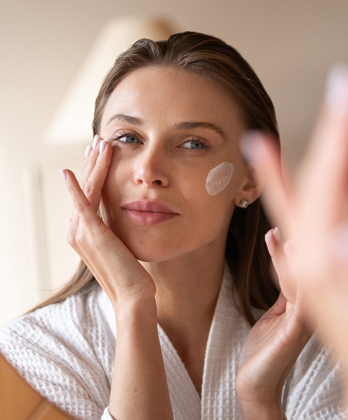 Woman applying skincare in front of a mirror.