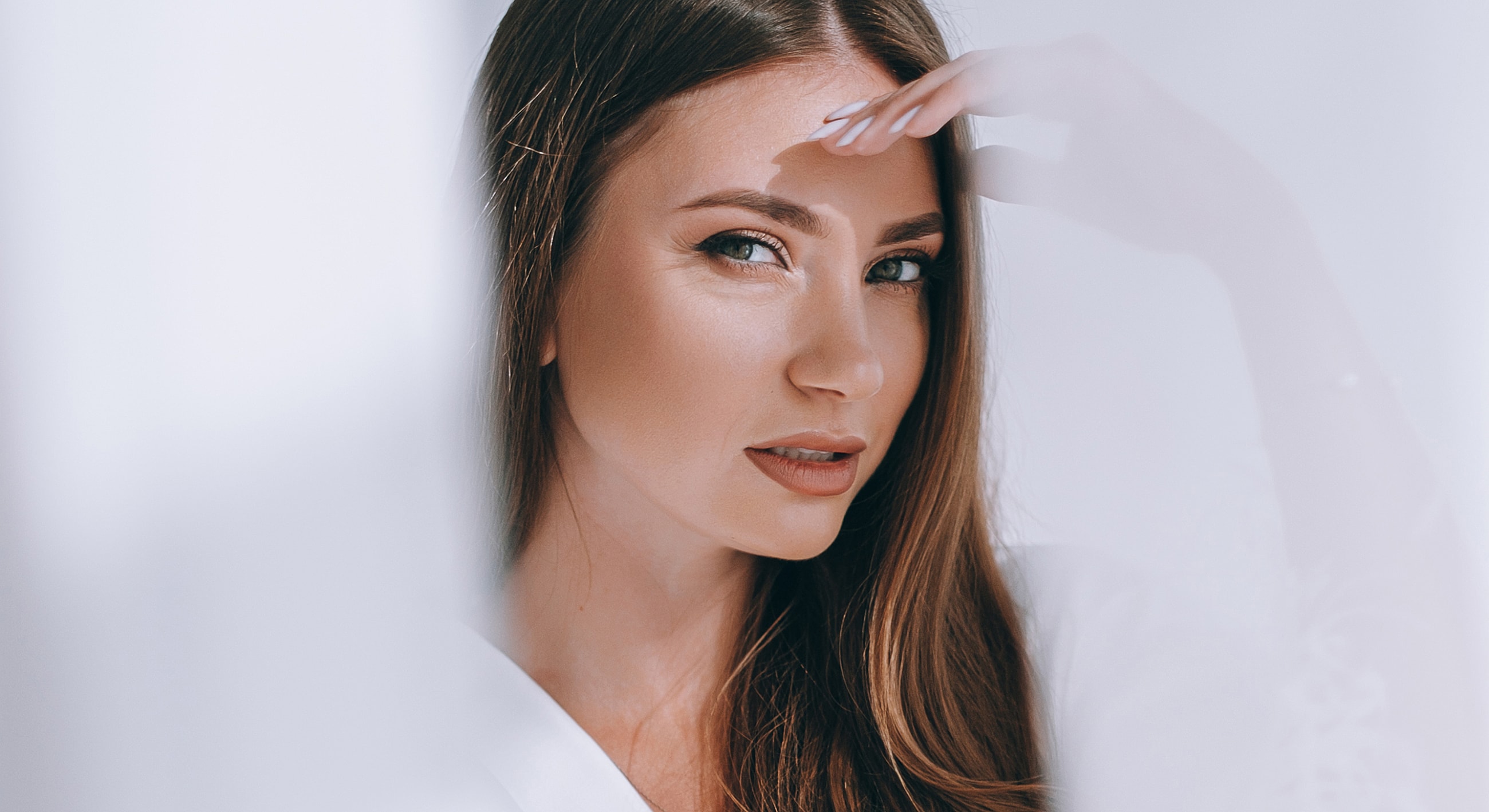 Woman looking through sheer fabric with soft lighting.